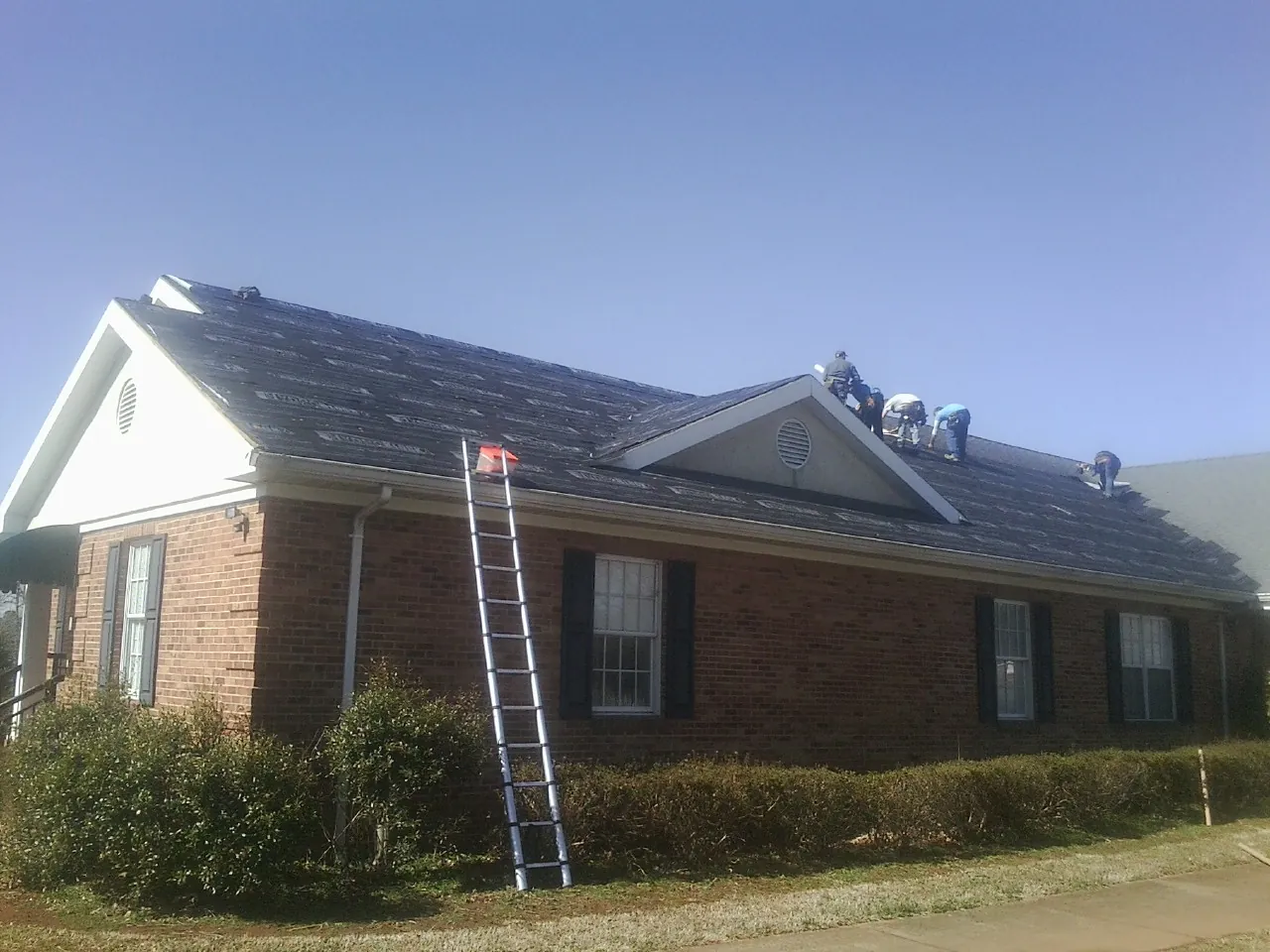 Crew tearing shingles off a brick ranch roof with a ladder set — Emergency Roof Repair work by our crew in Fallon