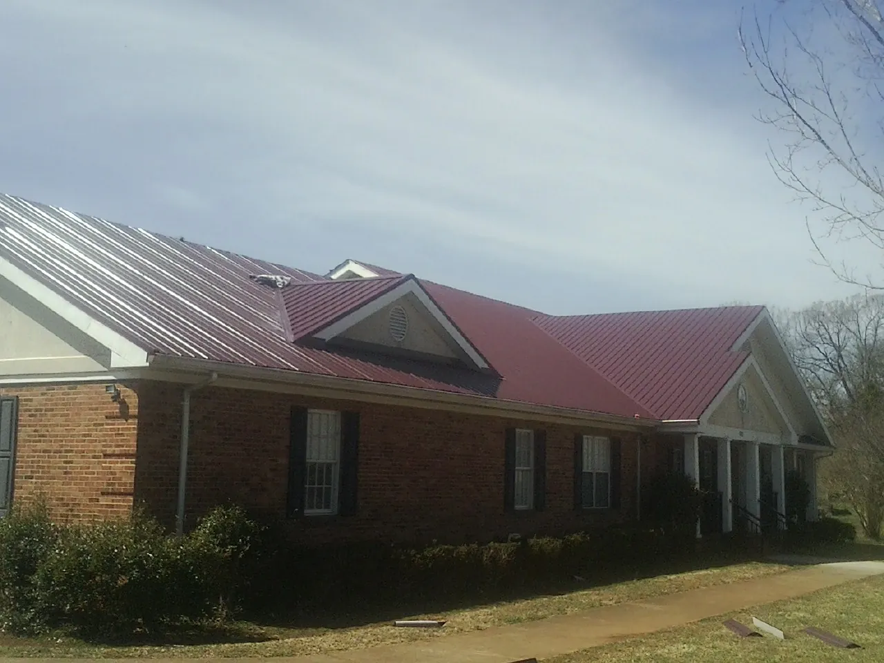 Red metal roof with gabled entries on a long brick building, from a Hail Damage Roof Repair job in Fallon