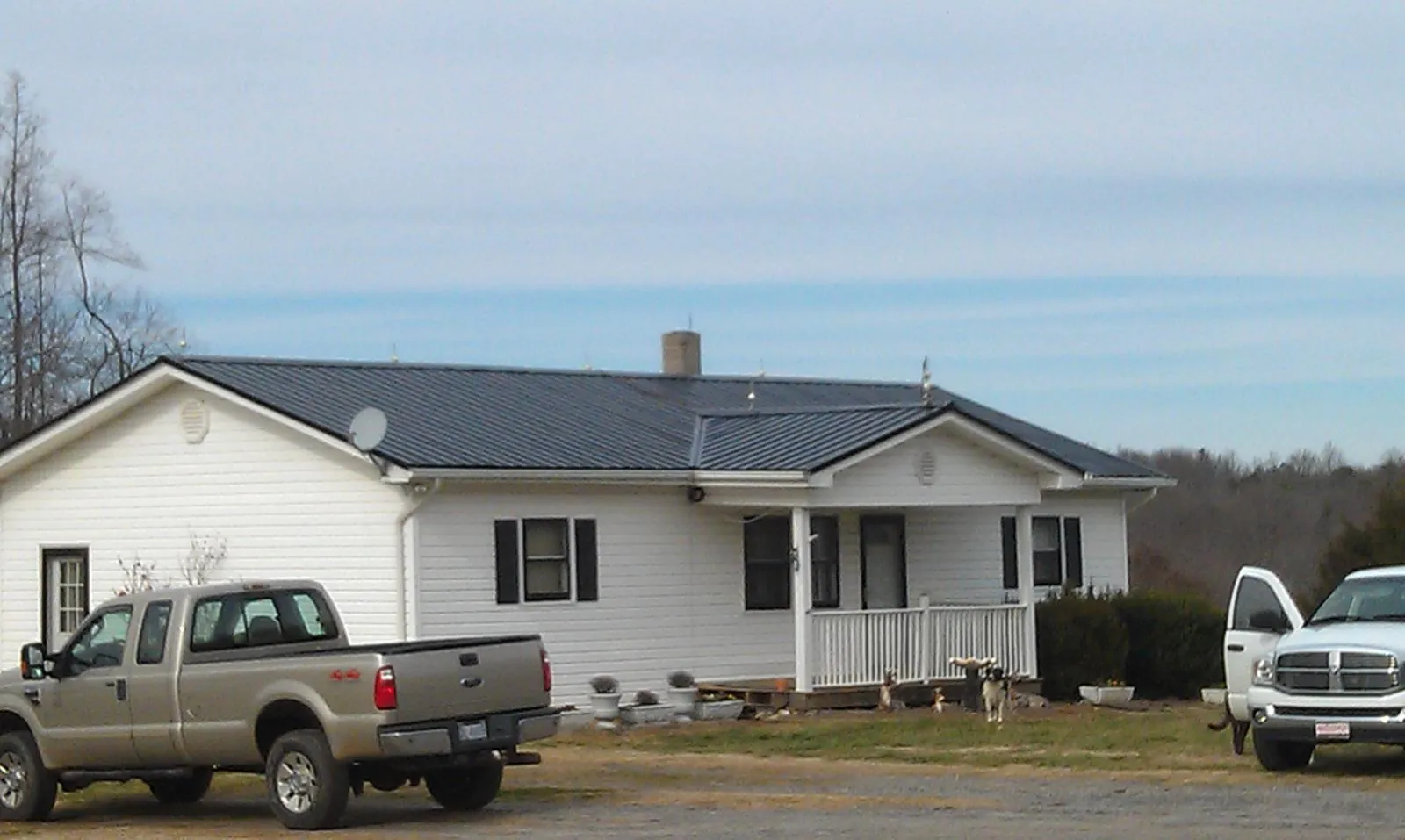 Finished dark metal roof on a white ranch home with work trucks parked in Fallon