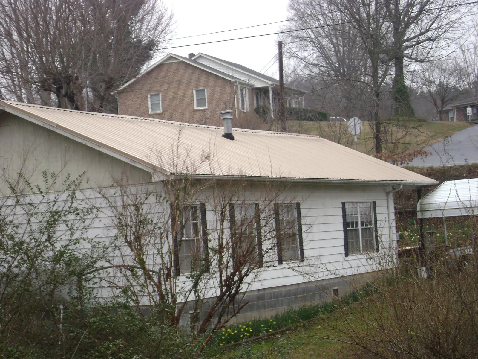 Tan metal roof on a white sided house set into a hillside — Commercial Roofing by Roofing Brothers in Fallon